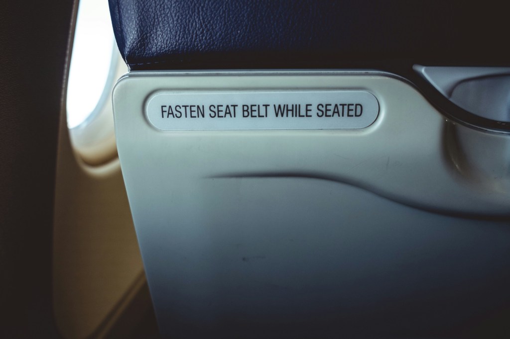 Close-up of an airplane seatback with a safety sign reading “Fasten Seat Belt While Seated.”